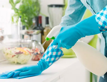 Person wearing blue cleaning gloves spraying a nondescript cleaning product