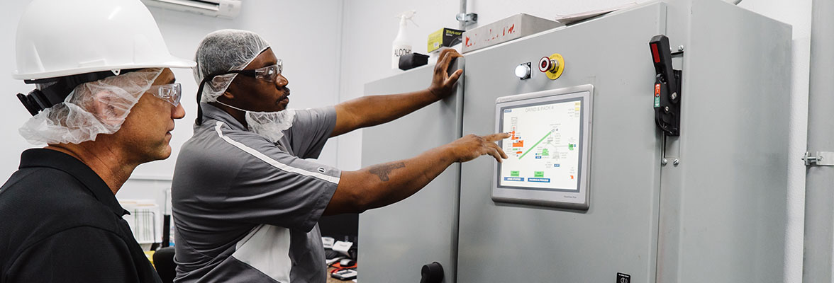 Two Kainos employees reading a screen on a large piece of equipment