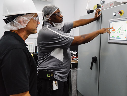 Two Kainos employees reading a screen on a large piece of equipment