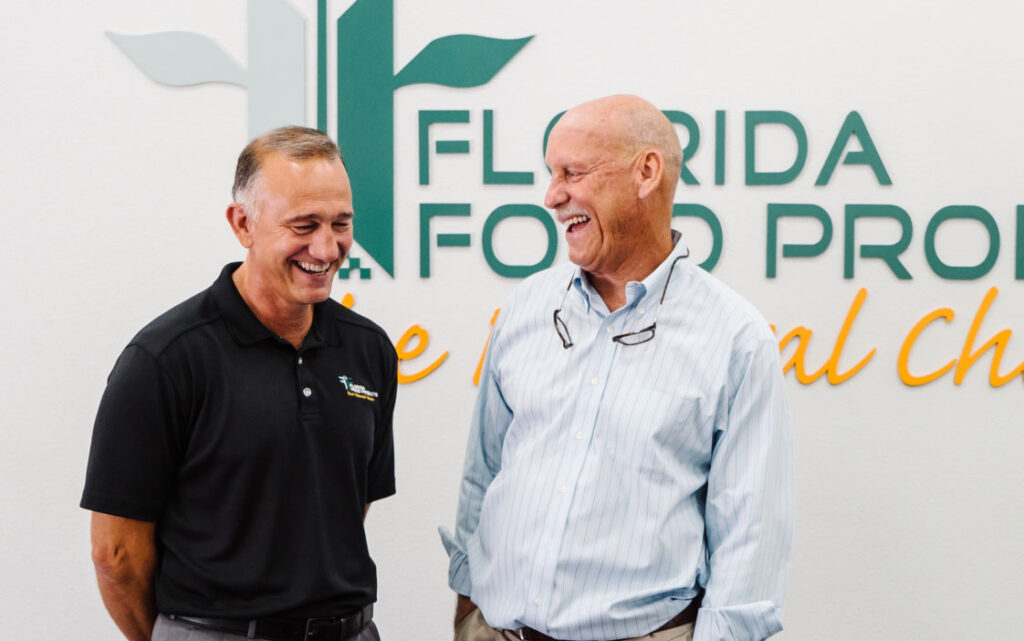 Two men in front of Florida Food logo on a wall